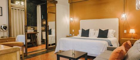 A hotel room with a large bed, a small table, a sofa, and a mirror.