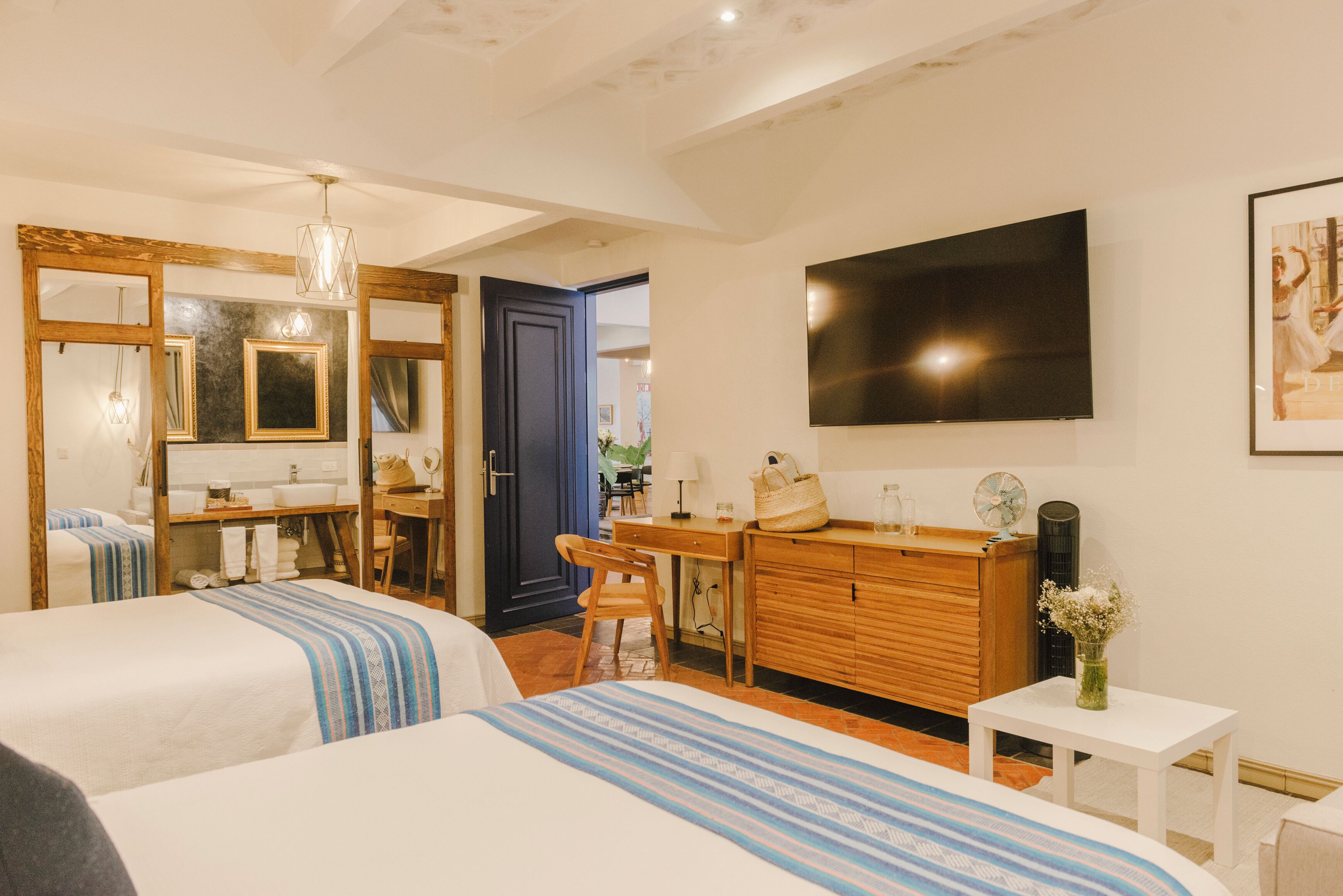 A hotel room with two beds, a wooden dresser, a TV, and a bathroom visible through an open door.