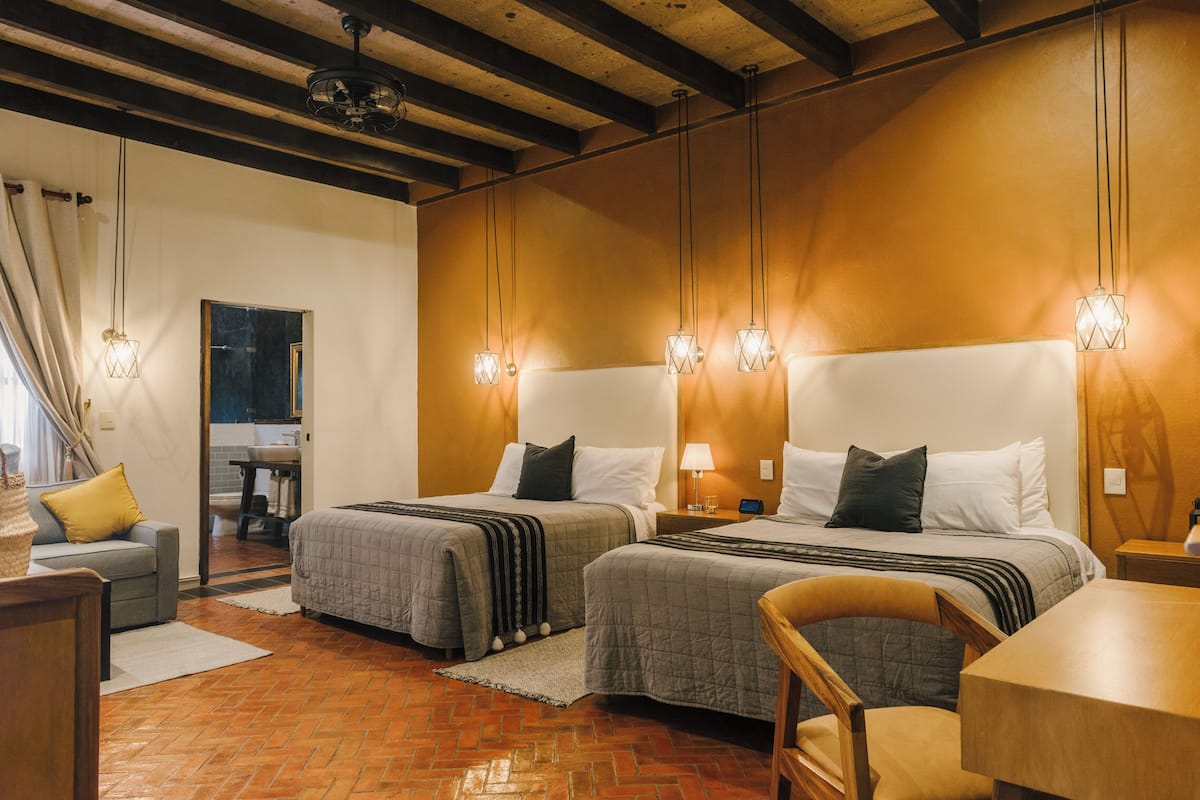 Une chambre d’hôtel avec deux lits, un plafond en bois et un sol en briques.