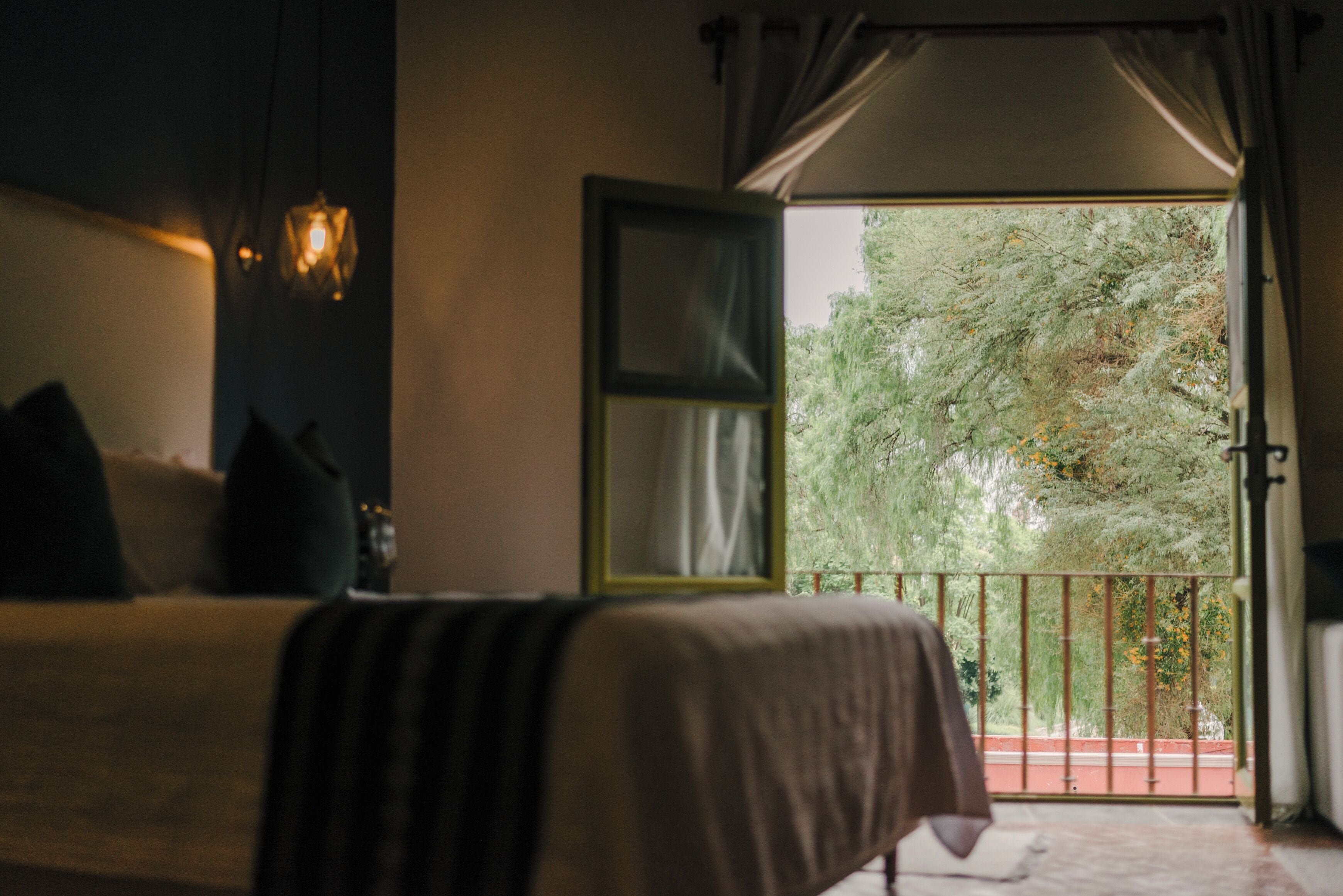 Un dormitorio con cama, una mesita de noche, un cuadro enmarco y un balcón con vistas a árboles.