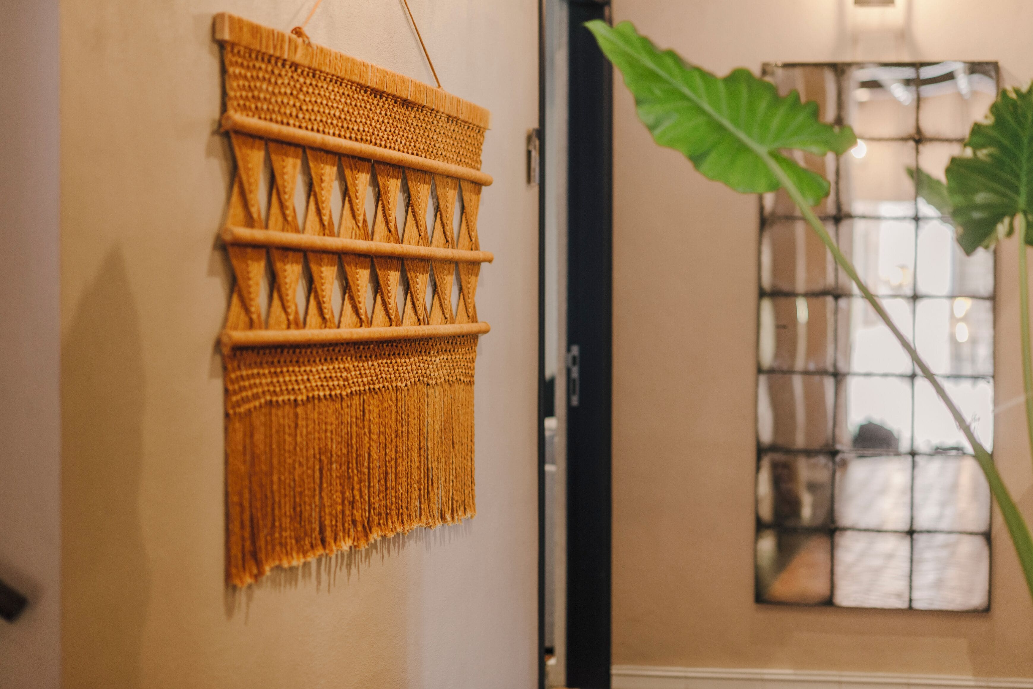 A wall hanging with a geometric pattern, a window with a grid design, and a plant with large leaves.