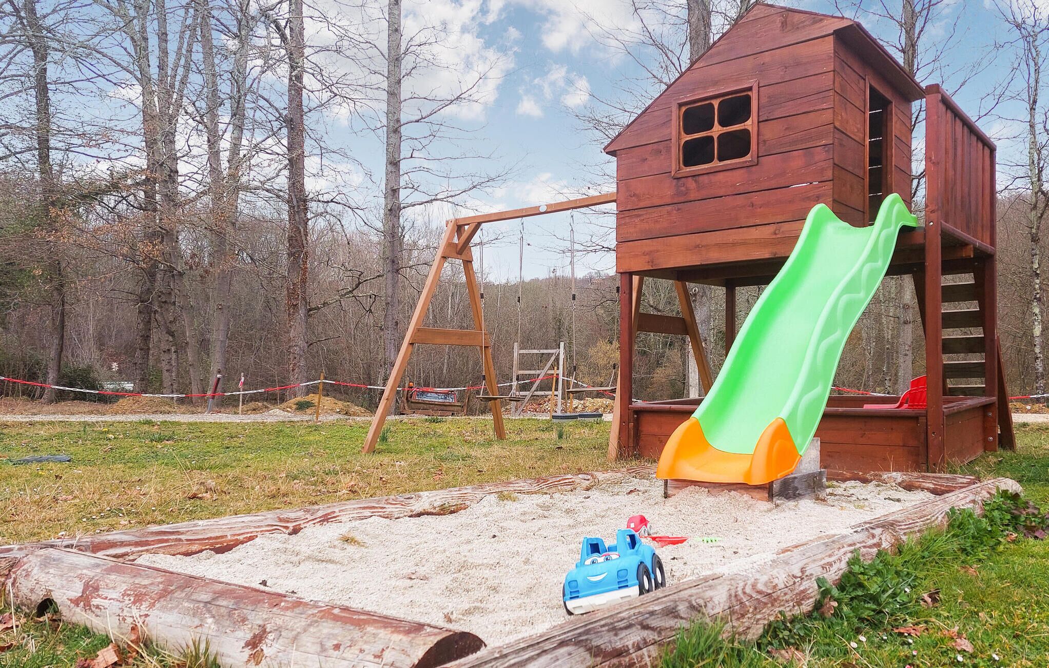 Une cabane en bois avec un toboggan et une balançoire, située dans un espace boisé.