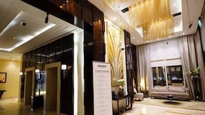 Un hall de hotel con mostrador de recepción, una zona de estar con sofá y sillones, y un gran ventanal con cortinas.