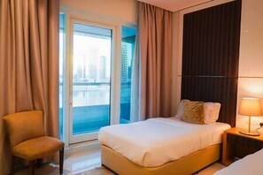A hotel room with a bed, a chair, a nightstand, and a view of a cityscape through a large window. - Magnificent 3 BR Canal Views (Dubai)