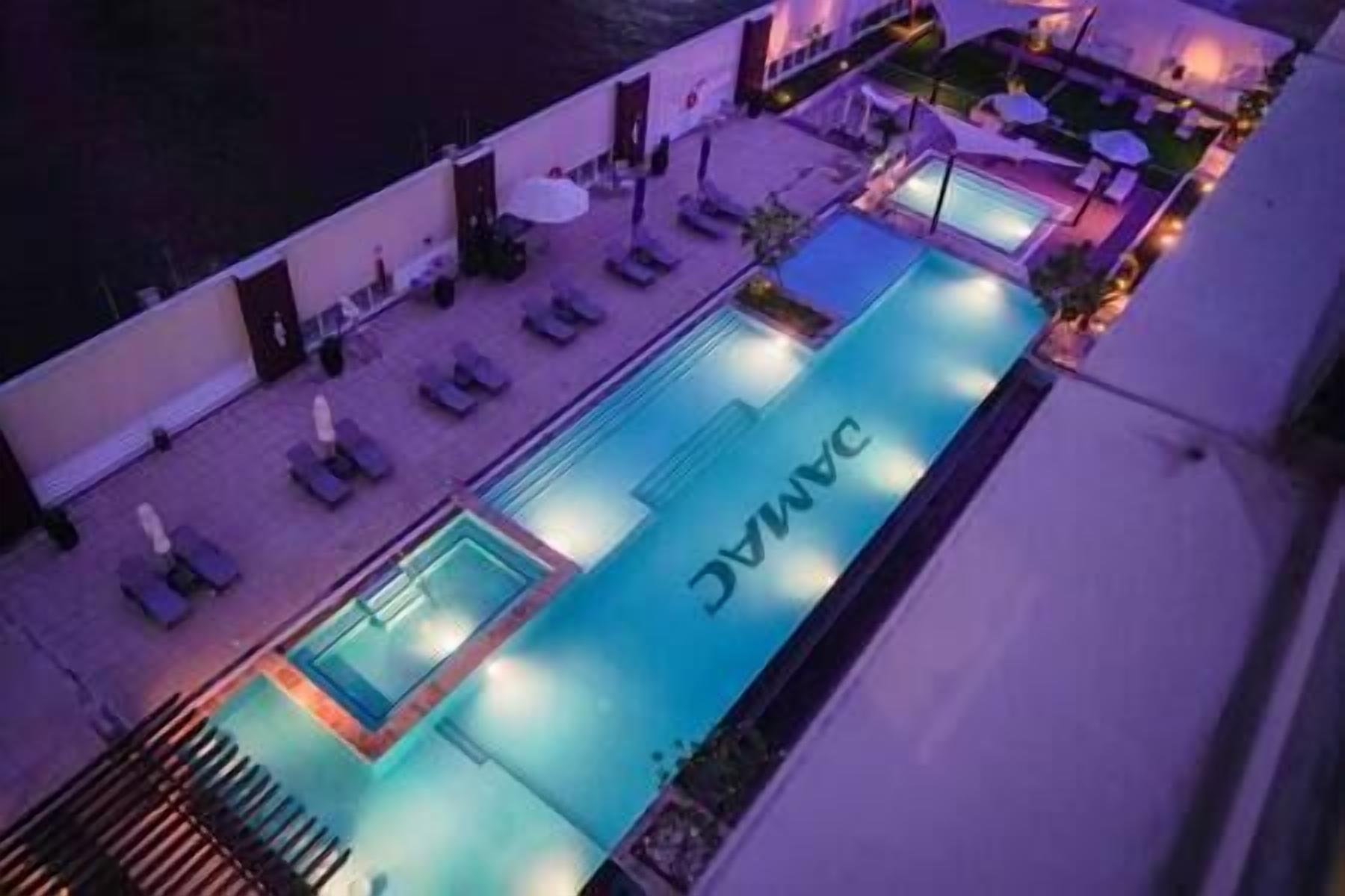 A pool area with lounge chairs and umbrellas, a sign reading "DANAC", and a view of the water.
