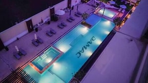 Zona de piscina con sillas de descanso y sombrillas, un letrero que dice "DANAC" y vista al agua.