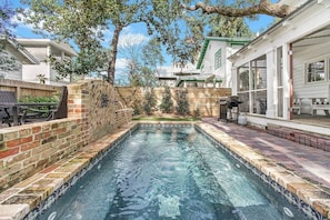 A swimming pool with a brick wall and a wooden deck, surrounded by a fence and trees.