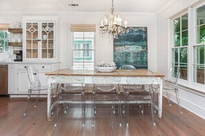 A dining area with a wooden table and chairs, a chandelier, and a large window with a view.