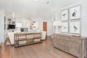 A room with a white sofa, a wooden coffee table, a white cabinet, and framed artwork on the wall. - Sugar Grove- 4 BR in Old Seagrove, Private Heated Pool, Steps to Beach and Seaside! (Seagrove Beach)