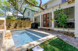 A backyard with a swimming pool, a wooden deck, and a small tree.