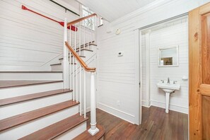 A staircase with wooden steps and white railings, leading to a room with a white wall and a wooden door.