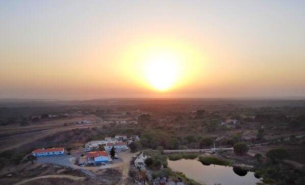A rural landscape with a small settlement, including houses and a pond, during sunset.