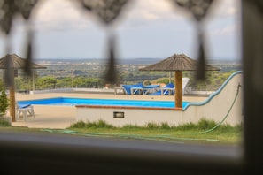A pool area with lounge chairs and umbrellas, surrounded by a view of a landscape.