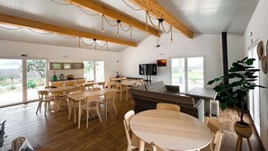 A spacious dining area with wooden tables and chairs, a large window with a view of the outdoors, and a television mounted on the wall. - Monte Sardinha (Santiago do Cacém)
