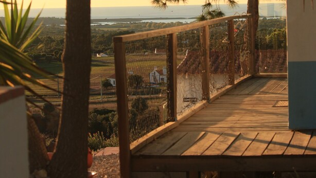 A wooden deck with a railing overlooking a landscape with trees and a distant view of a bridge. - Monte Sardinha (Santiago do Cacém)