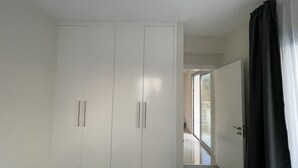 Una habitación con un armario blanco grande, una puerta que da a otra estancia y una cortina negra.