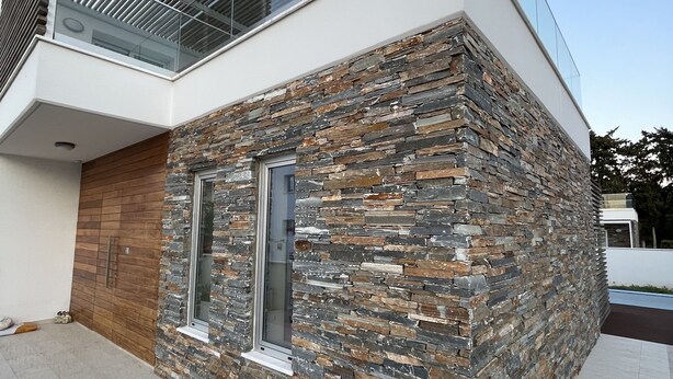 Una casa moderna con fachada de piedra, puerta de madera y balcón de cristal.