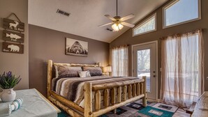 Une chambre avec un lit en bois, un ventilateur de plafond, une fenêtre avec des rideaux légers et un panneau mural décoratif représentant des silhouettes d’animaux.