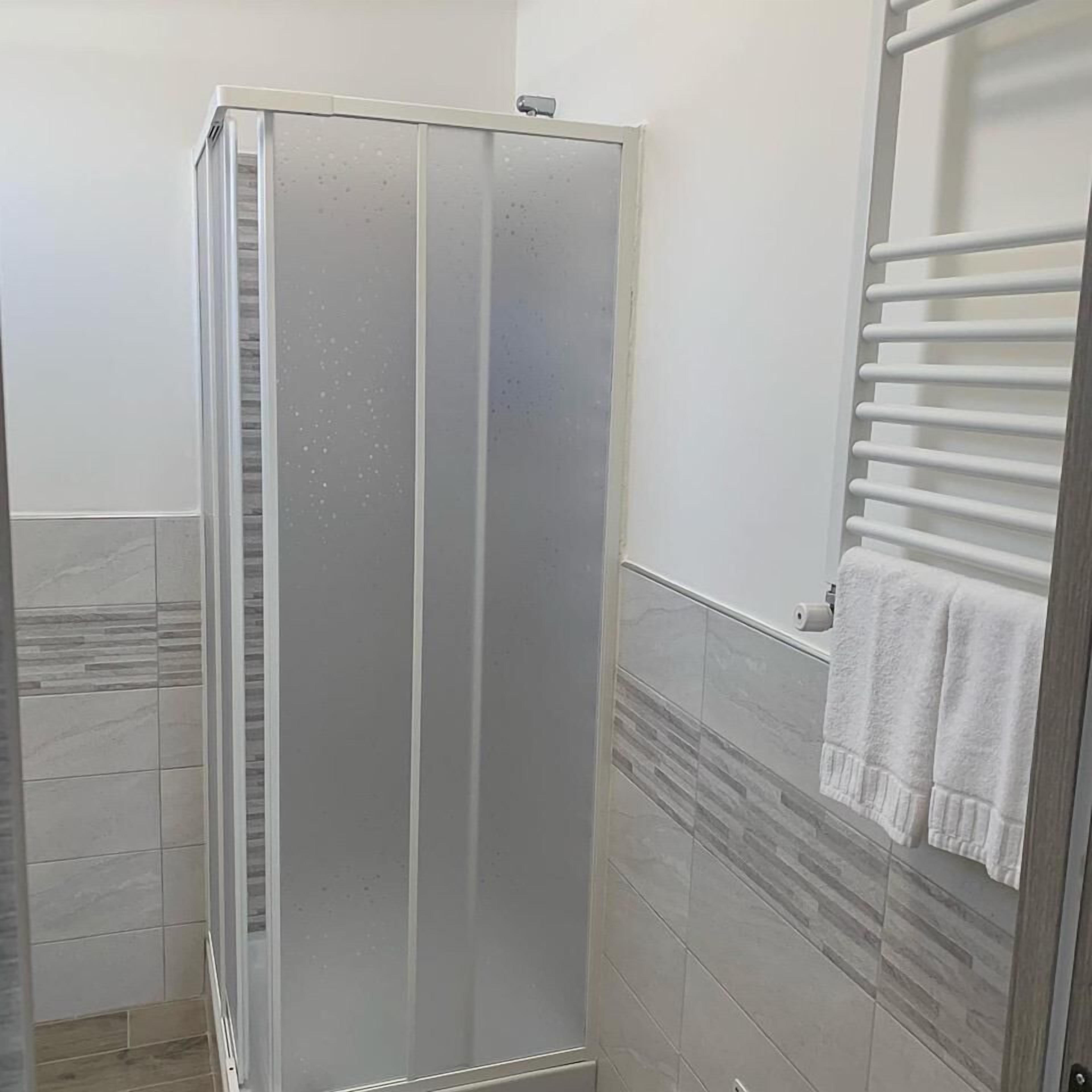 Une salle de bain avec une douche à parois de verre, des murs carrelés et un porte-serviettes.