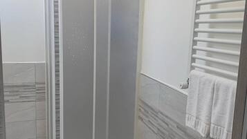 Une salle de bain avec une douche à parois de verre, des murs carrelés et un porte-serviettes.