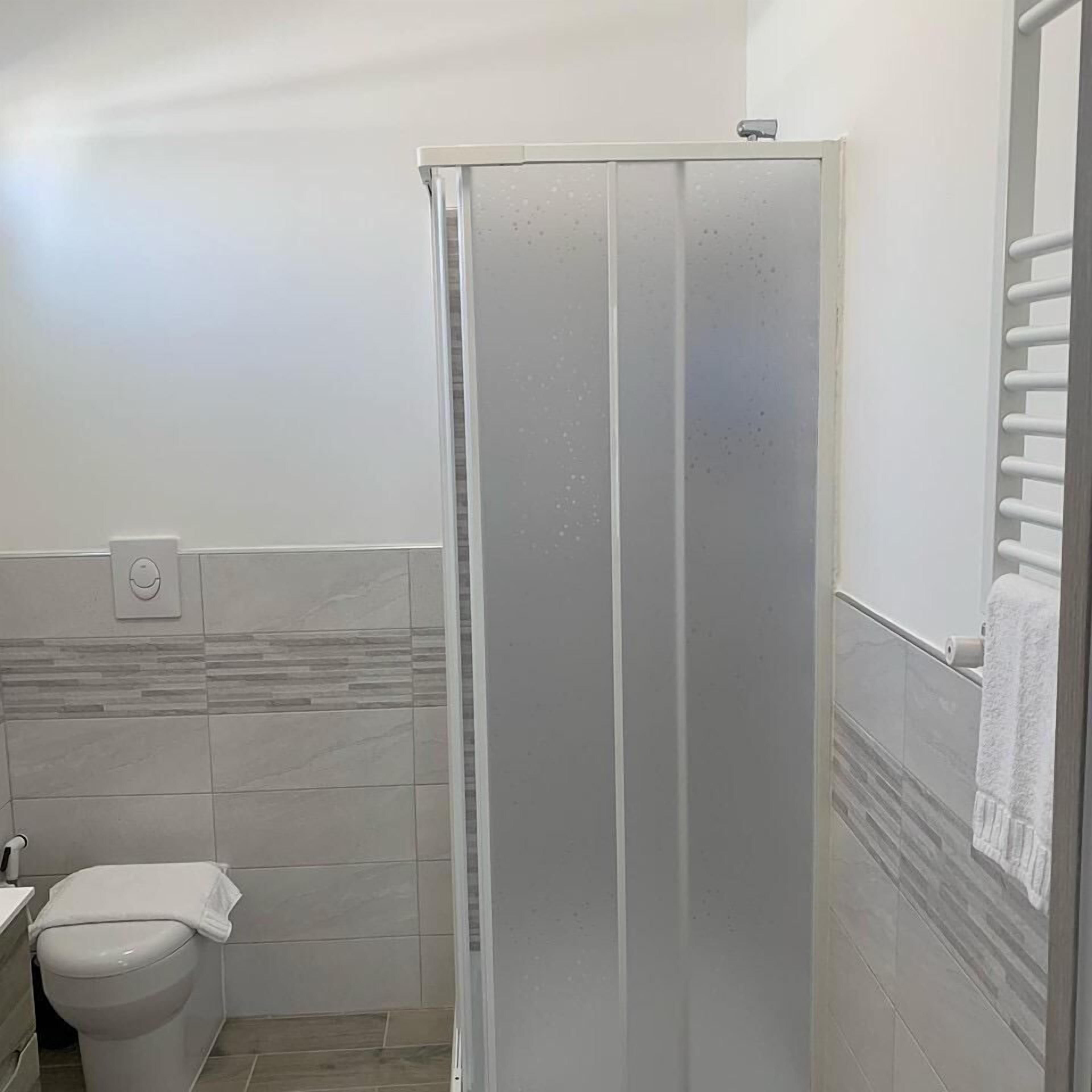 Un baño con inodoro, cabina de ducha y barra para toallas.