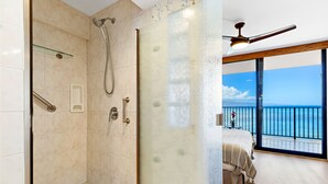 Un baño moderno con cabina de ducha de vidrio, un balcón con vistas al océano y un ventilador de techo.