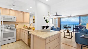 Una cocina moderna con una isla central, armarios de madera y vistas al océano a través de amplios ventanales.