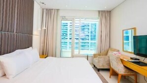 A hotel room with a large bed, a desk with a computer, a chair, and a view of a building through the window. - Splendid1BRapartmentinCanalViews (Dubai)