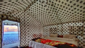 A tented room with a bed, a window, and a view of a mountainous landscape. - World Attic Camp (Leh)