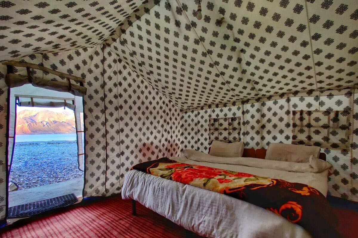 A tented room with a bed, a window, and a view of a mountainous landscape.