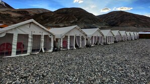 A row of white tents with numbered doors, set on a rocky terrain with mountains in the background. - World Attic Camp (Leh)