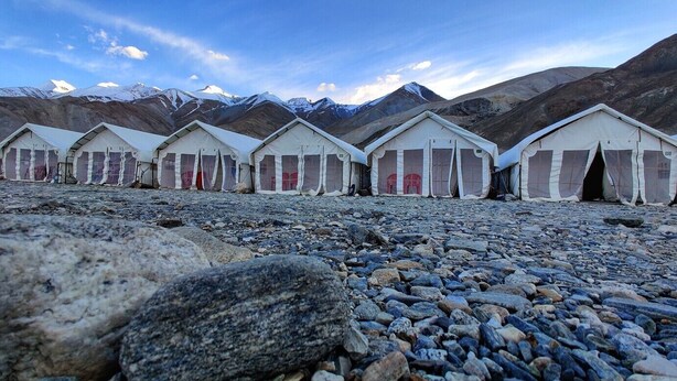 A row of white tents with red doors, set on a rocky terrain with mountains in the background. - World Attic Camp (Leh)