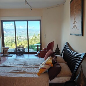 Una camera da letto con un letto grande, una poltrona rossa, un tavolino e vista su un paesaggio attraverso una porta scorrevole.