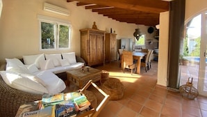 A cozy living room with a sofa, a coffee table with books, a wooden cabinet, and a dining area with chairs and a table. - Pretty, luxurious villa with private pool and superb view (Dénia)
