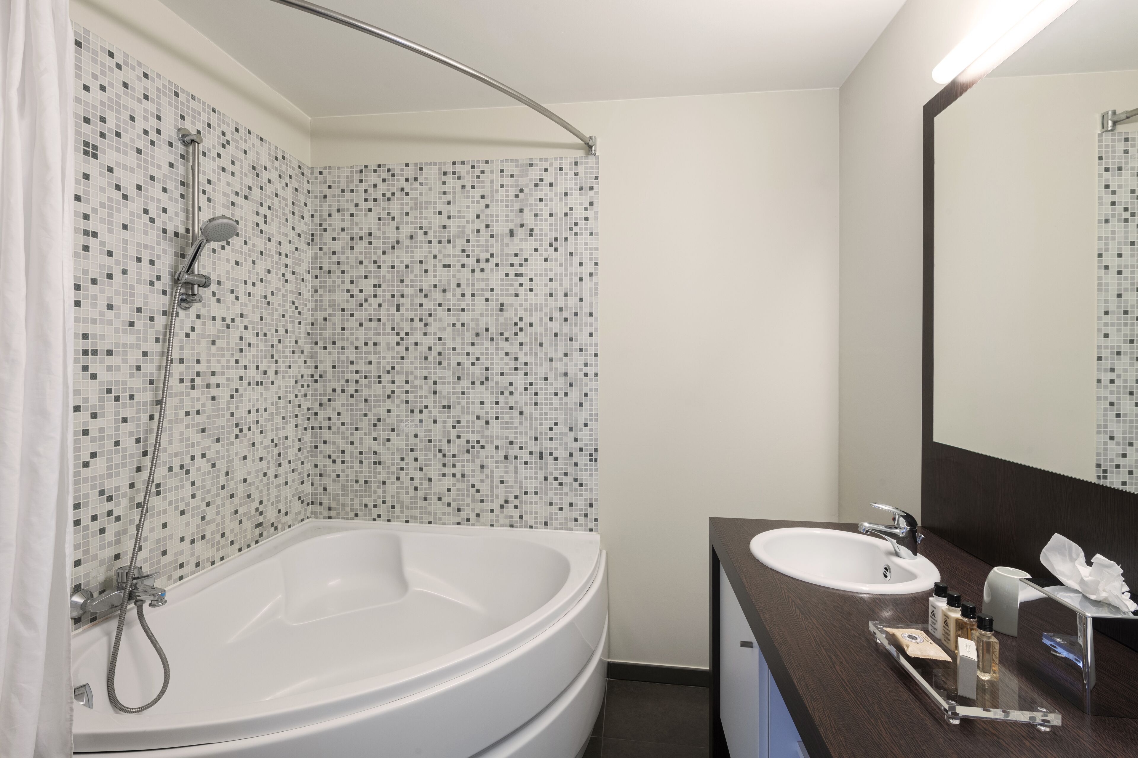 Une salle de bain moderne avec un mur de douche recouvert de mosaïques, une baignoire sur pieds et un meuble-lavabo avec un miroir.