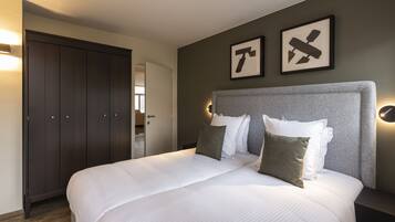Una cama bien hecha con sábanas blancas y dos almohadas, un armario de madera oscura y dos cuadros en la pared.