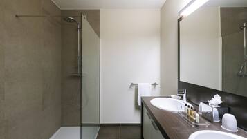 Un baño moderno con cabina de ducha de vidrio, un lavabo blanco y un espejo grande.