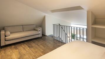 A modern loft bedroom with a wooden floor, a beige sofa, a white bed, and a balcony with a railing.