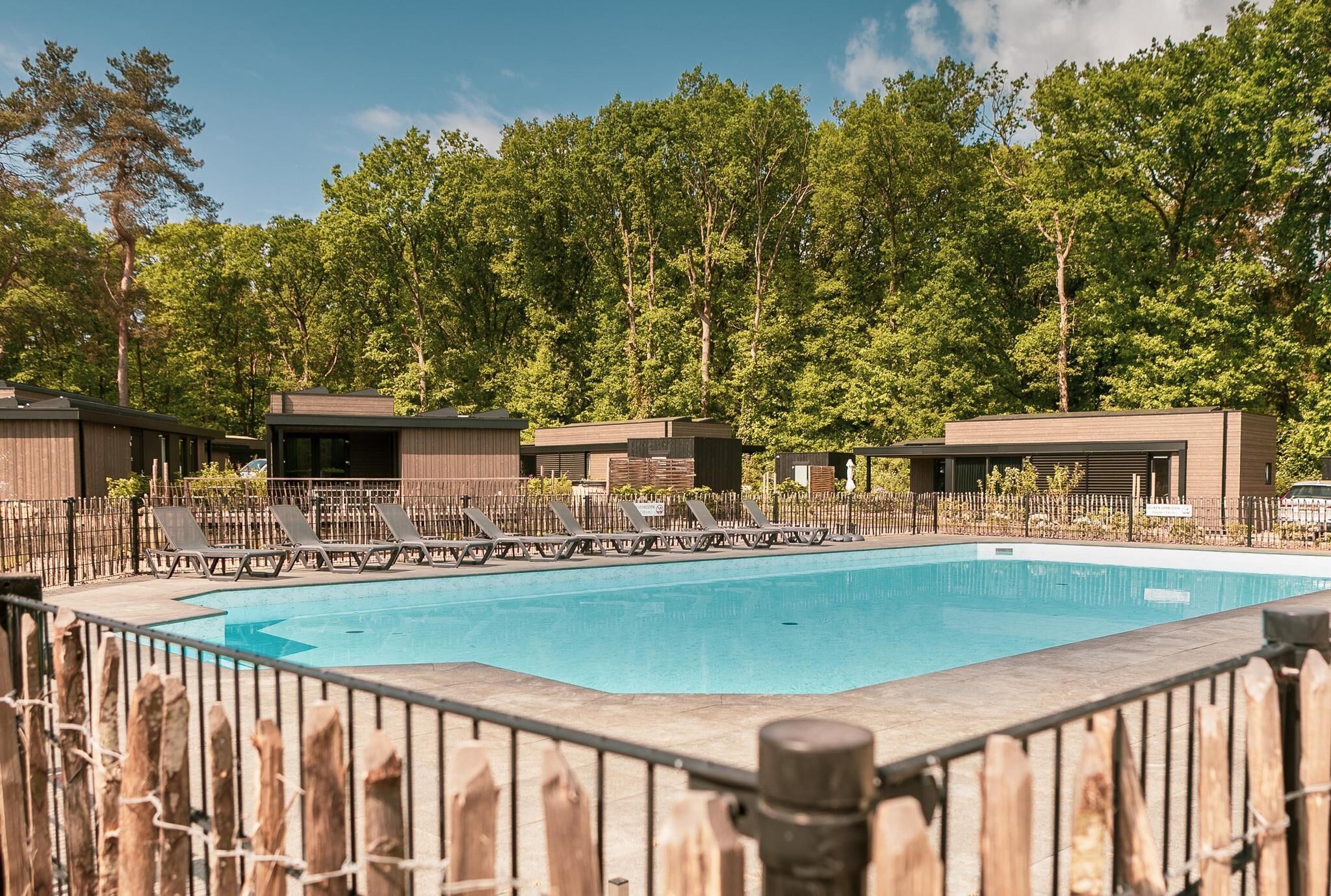 A swimming pool with lounge chairs and wooden cabins in a wooded area.