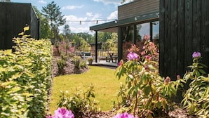 A modern building with a glass facade, a wooden deck, and a well-maintained garden with various plants and flowers.