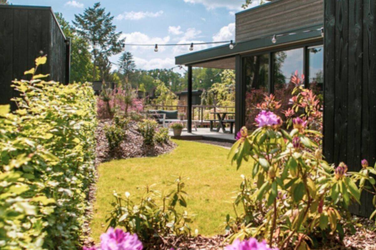 A modern building with a glass facade, a wooden deck, and a well-maintained garden with various plants and flowers.