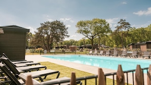 A swimming pool with lounge chairs and a wooden building, surrounded by trees.
