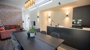 A modern living space with a dining area, a kitchen with a built-in oven, and a red sofa.