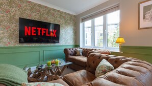 Una sala de estar con pared verde, un sofá de cuero marrón, una mesa de centro de vidrio y un televisor mostrando "NETFLIX".