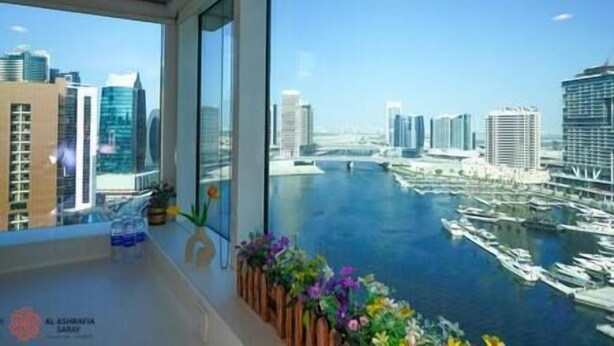 Habitación de hotel moderna con un ventanal grande que da a un puerto deportivo y un paisaje urbano.