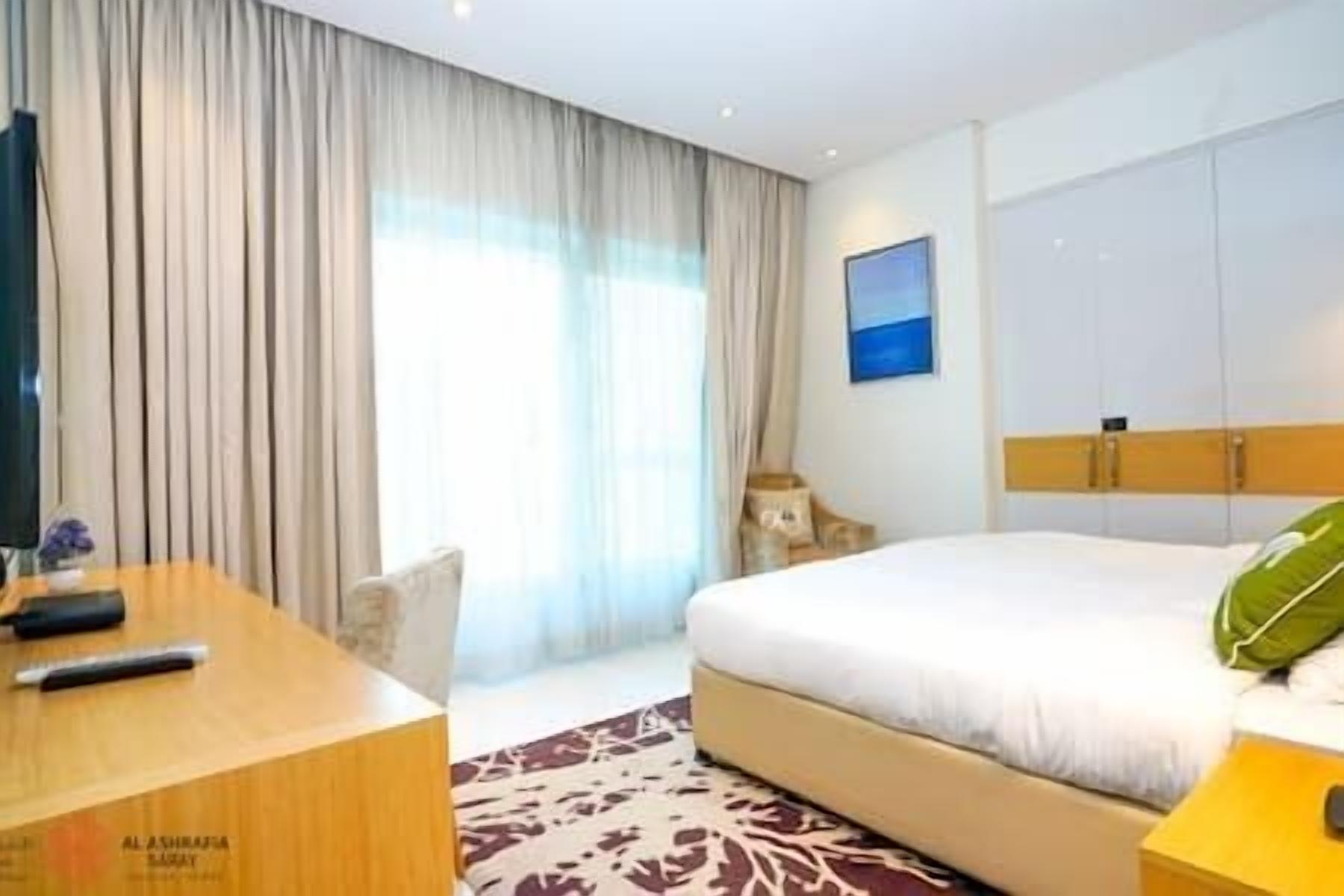 A hotel room with a bed, a desk, a chair, and a window with curtains.