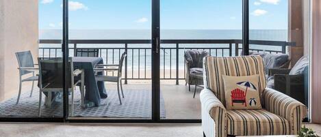 Un balcón con vistas al océano, una mesa con sillas y sillones a rayas.