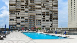 A high-rise building with multiple balconies, a swimming pool, and outdoor seating areas.