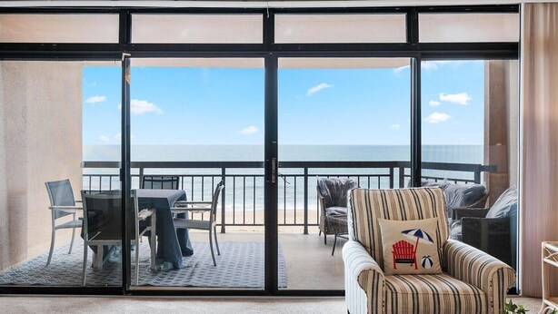 A balcony with a table and chairs, a striped armchair, and a view of the ocean.