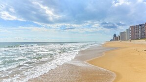 A beach with a sandy shore, waves, and a city skyline in the background.